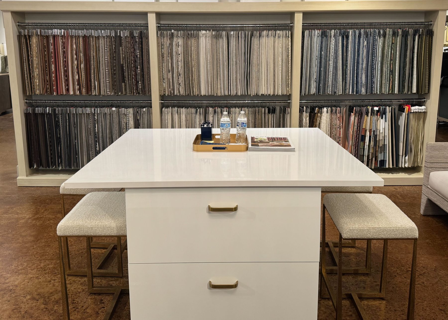 Fabric station with a white work island and stools in front of a wall of hanging upholstery samples